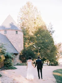 Bride and groom walking hand in hand away from the stone estate, framed by mature trees, from a Santa Barbara wedding editorial by Yuliya Supin Design