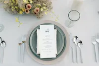 Detailed reception place setting featuring layered dinnerware, menu card, and florals inspired by vineyard landscape.