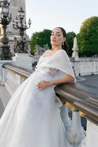 Fashion portrait of the bride standing on the Pont Alexandre III bridge wearing pearl earrings and an embroidered gown.
