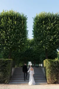 Bride and groom walking up garden stairs in Paris surrounded by groomed trees and historic architecture