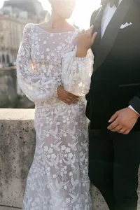 Close portrait of the bride and groom holding hands at sunset with details of the bride’s embroidered gown visible.
