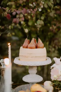 Wedding cake topped with poached pears held by guest in outdoor reception setting