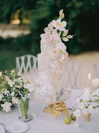 Two-tier hand-painted floral wedding cake on a gold stand, styled with grapes and greenery for a Santa Barbara wedding editorial by Yuliya Supin Design