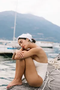 Model sitting on wooden dock at Lake Como in minimal bridal styling during fashion editorial shoot
