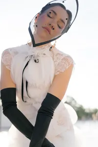 Close portrait of a bride in Paris with eyes closed, wearing a couture gown, black gloves, and a sheer polka-dot headpiece, creating a soft and emotional fashion editorial moment.