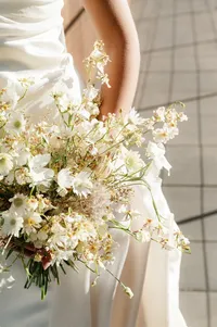 Close-up of bride’s lace gown, hand detail, and bouquet in soft natural light.