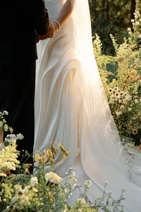 Close-up of bride and groom holding hands during the ceremony as warm sunset light illuminates her gown.