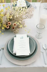 Close-up of reception table featuring green stone plate, wooden charger, silver flatware, blue glassware, velvet linen, and florals inspired by sheep texture.