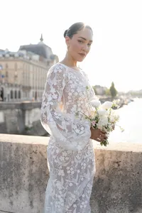 Bride standing on a Paris bridge at sunset holding bouquet with the Seine River and historic architecture behind her.