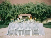 Vintage bistro chairs trailing white ribbon, lined along a linen-draped reception table, styled for a Santa Barbara wedding editorial by Yuliya Supin Design