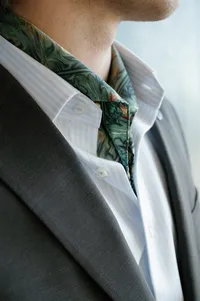 Close-up of groom’s rehearsal dinner look featuring tailored jacket, scarf, and shirt detail.