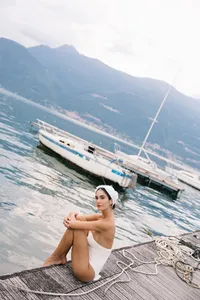 Model sitting on dock by Lake Como with mountains in background during fashion editorial
