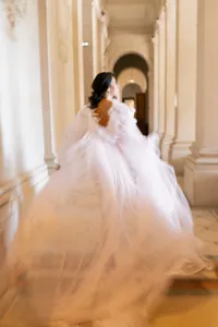 Bride in a voluminous tulle gown moving through the colonnaded hallway of Château de Ferrières