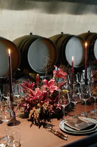 Refined rehearsal dinner place setting with burgundy florals, candles, and layered dinnerware designed for an intimate winery celebration.
