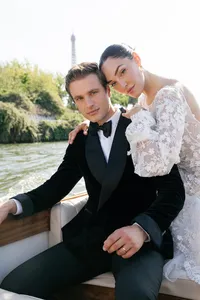 Close portrait of the bride and groom seated in a boat on the Seine River in Paris, holding hands as the bride leans toward the groom with the Paris river landscape behind them