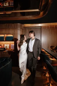 Bride and groom walking hand in hand toward rehearsal dinner in a moody speakeasy setting.