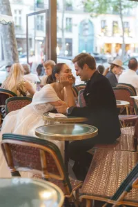 Bride and groom laughing together at their café table in Paris as they hold hands and share a playful moment.