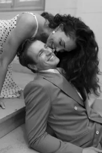 Black and white portrait of the bride and groom laughing together on a staircase as the bride playfully leans toward the groom from behind during their engagement session in Paris.
