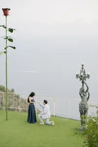 Man kneeling to propose on a lawn above the Mediterranean, beside a giant rose sculpture, Èze