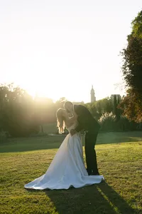 Bride and groom backlit by the setting sun on a garden lawn