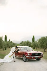 Bride and groom with a vintage red car on a cypress-lined road