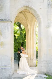 Bride and groom standing under a stone archway opening onto a garden,