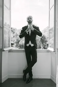 Groom in a suit standing by a tall window before the ceremony