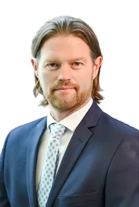 Headshot of an executive in a tie and blazer, serious pose, neutral backdrop