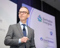 A man in a grey suit and navy polka-dot tie speaks on stage at the Bankable Energies conference, with the event branding and Close Brothers sponsor logo visible on the backdrop behind him.