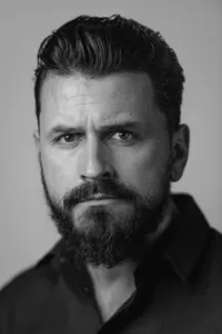 Professional headshot of a man with soulful expression, studio lighting, plain backdrop