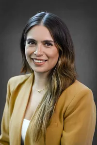 Corporate headshot of a business professional in a light yellow suit, grey backdrop