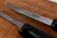 Two thin knives laying next to each other on a cutting board