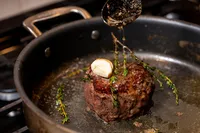 Butter being basted over a small steak in a pan