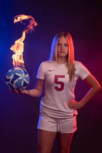 A person in a soccer jersey holding a ball that is on fire with one hand and pointing to their number on their back with the other