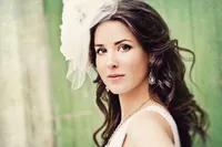 Romantic bridal portrait of a woman with soft curled hair, wearing a sheer tulle headpiece and drop earrings, captured in natural light with a timeless editorial style.