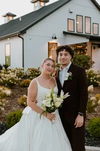 Couple posing in front of a bunch of flowers looking at the camera