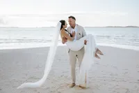 Groom carries bride in long viel in the middle of The Exumas surrounded by blue water