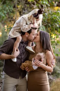 Couple sharing a kiss with newborn resting in mom arms during an outdoor family photography session by Lauren Ford Photography in Orange County