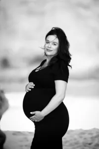 Black and white image of a woman in a dress showcasing her baby bump during a maternity session in Orange County
