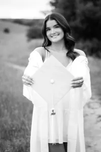 Black and white image of a senior smiling while holding her graduation cap during a graduation photo session in Orange County