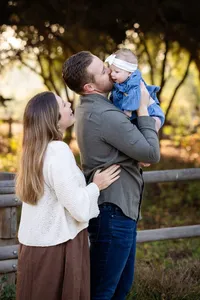 baby girl in dads arms while mom smiles behind him during an outdoor newborn session in Orange County