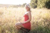 High school senior smiling in a red dress and cowboy boots during a graduation photo session in Orange County