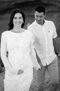 Pregnant woman smiling while holding her husbands hand and smiling at the camera during a maternity session in Orange County