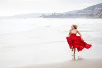girl running at the beach with a red dress during a graduation photo session in Orange County