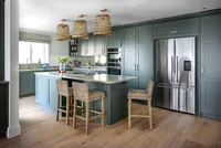 Interior photograph of a contemporary kitchen with green cabinetry, a central island and woven pendant lights.