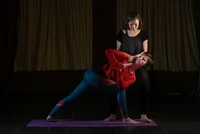 Two women practise yoga at the Devon School of Yoga, with one gently supporting the other in a pose.