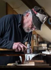 Guitar maker working on an acoustic guitar at the Brook Guitars workshop in Devon.