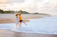 Two sisters laughing and kicking through the surf as they splash along the shoreline during a family beach portrait session. (Photographed by Nature's Child Photography)
