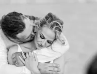 St. Augustine Beach, wedding capturing a bride and groom in a close embrace in a black and white, the groom kissing her neck as wind lifts her hair. - A portrait experience by Nature's Child Photography.