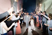 Jacksonville, FL wedding photographers photographing in St. Augustine, wedding capturing a bride and groom walking hand in hand through a nighttime sparkler exit, guests lining the walkway and celebrating around them.